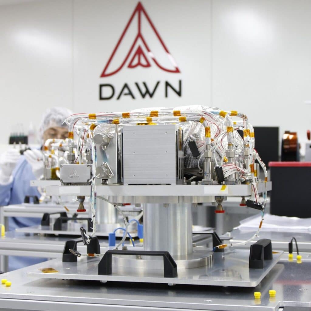 Laboratório da Dawn Aerospace, com destaque para um módulo em desenvolvimento. Equipamentos de alta tecnologia estão visíveis ao redor, evidenciando a inovação e o progresso em pesquisa e desenvolvimento no setor aeroespacial.