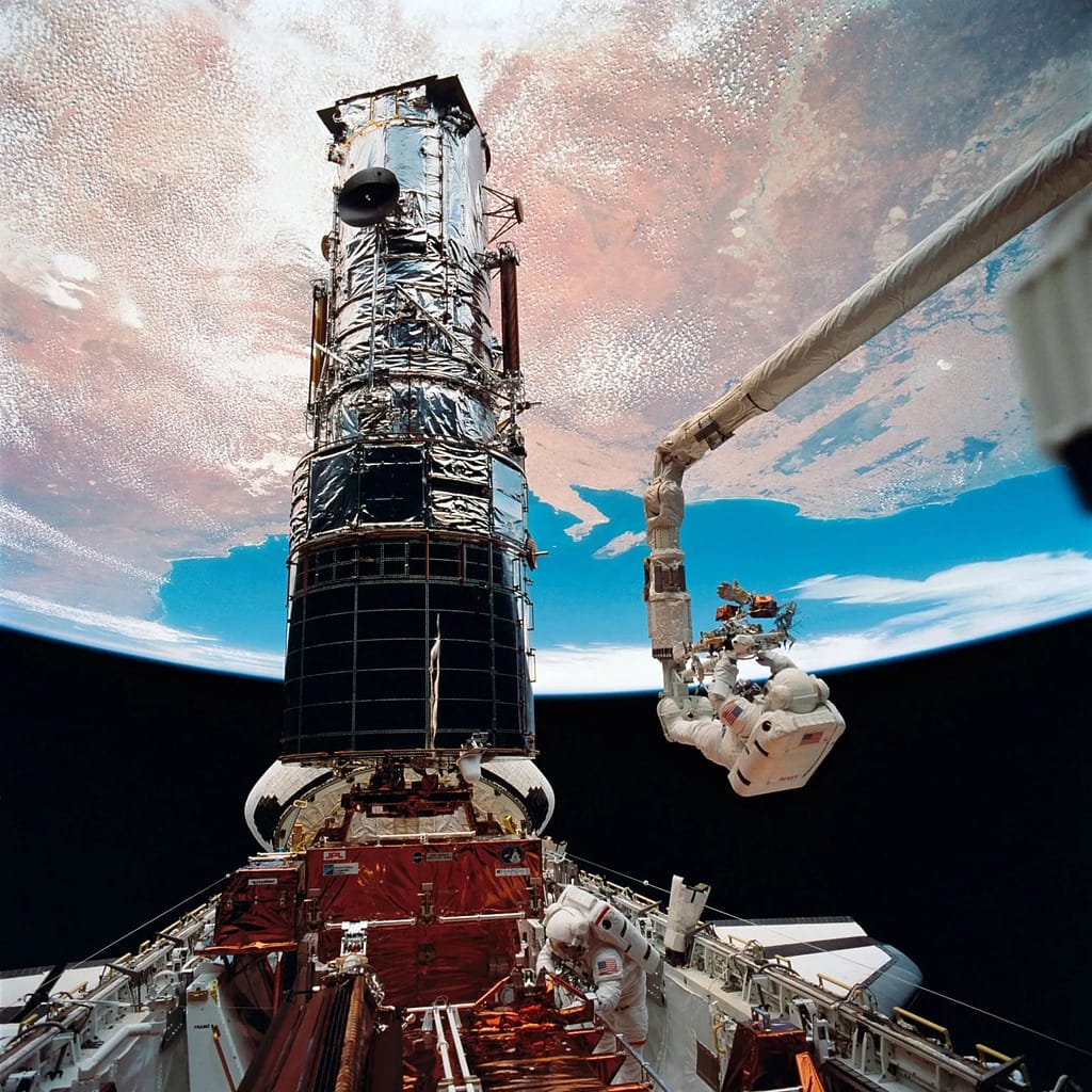 O astronauta F. Story Musgrave, ancorado na extremidade do braço do Sistema de Manipulação Remota (RMS), prepara-se para ser elevado ao topo do imponente Telescópio Espacial Hubble para instalar capas protetoras nos magnetometros. O astronauta Jeffrey A. Hoffman (parte inferior da imagem) auxiliou Musgrave nas tarefas finais de manutenção do telescópio, concluindo sua primeira missão de manutenção (SM 1).
NASA