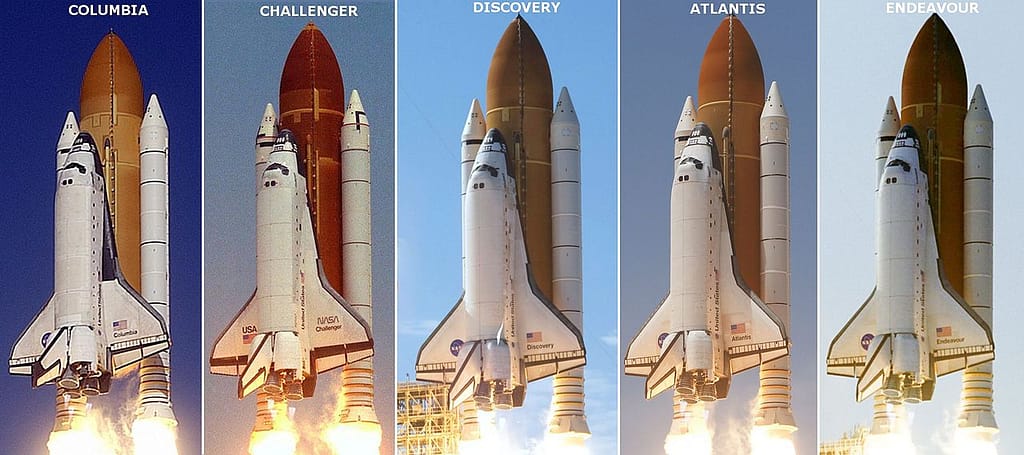 Imagem histórica mostrando diversos ônibus espaciais da NASA alinhados lado a lado em uma base aérea. As naves, com suas fuselagens brancas e pretas, destacam-se contra o céu limpo e o chão de concreto. Ao fundo, veículos de apoio e técnicos dão escala à grandiosidade dessas máquinas que marcaram a era dos voos espaciais tripulados.