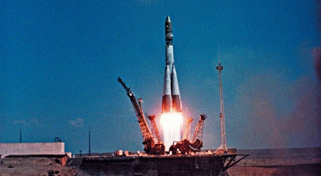 A espaçonave Vostok 1, com Yuri Gagarin a bordo, é lançada do Cosmódromo de Baikonur em 12 de abril. O foguete sobe em meio a uma enorme nuvem de fumaça e chamas, marcando o início do primeiro voo tripulado ao espaço e um momento histórico para a exploração espacial.