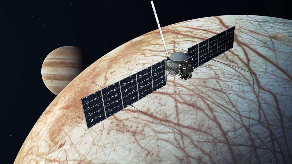 alt="Uma nave espacial paira sobre uma lua listrada avermelhada com o planeta Júpiter ao fundo."