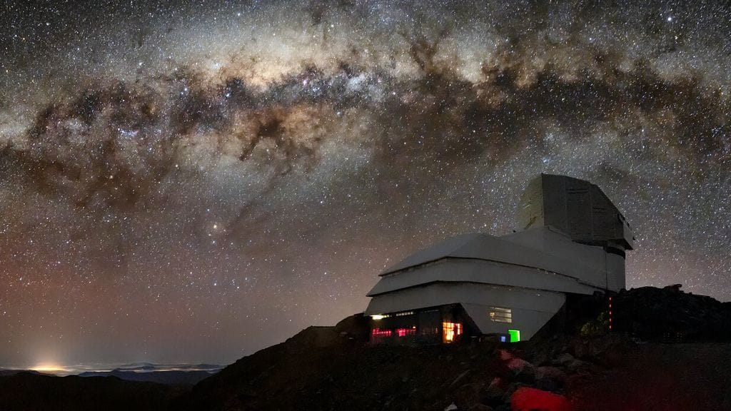 Observatório Vera C. Rubin sob um céu noturno repleto de estrelas e a Via Láctea visível ao fundo, no Cerro Pachón, Chile.