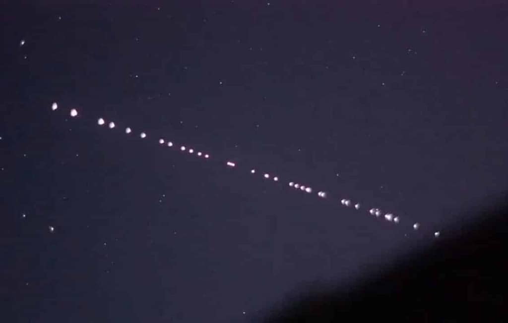 Fotografia real de satélites Starlink em órbita, visíveis no céu noturno como uma linha de pontos brilhantes, formando um padrão semelhante a um 'trenzinho'. A imagem mostra os satélites da SpaceX enquanto viajam em conjunto, iluminando o céu escuro. Esse fenômeno é uma visão única e impressionante da constelação de satélites Starlink em movimento, conectando a Terra com sua rede global de internet via satélite.
