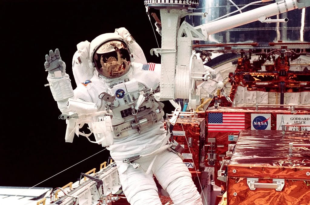 Steven L. Smith acena para seus companheiros de tripulação na cabine da Discovery enquanto trabalhava no terceiro dia de atividade extraveicular (EVA) para fazer a manutenção do Telescópio Espacial Hubble em fevereiro de 1997. NASA