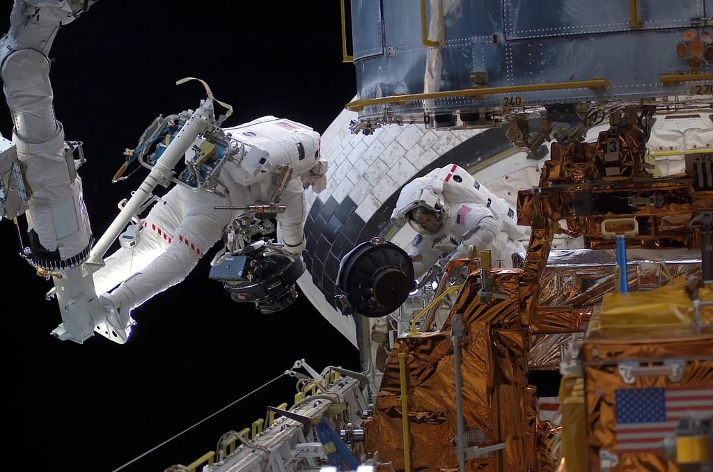 Steven L. Smith acena para seus companheiros de tripulação na cabine da Discovery enquanto trabalhava no terceiro dia de atividade extraveicular (EVA) para fazer a manutenção do Telescópio Espacial Hubble em fevereiro de 1997. NASA