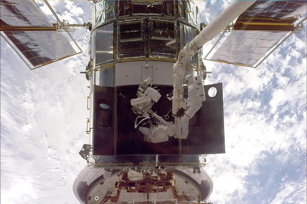 Steven L. Smith (à direita) e John M. Grunsfeld (à esquerda) usam o braço robótico RMS para executar tarefas de manutenção no Telescópio Espacial Hubble (HST) temporariamente.
capturado durante a terceira missão de manutenção do HST (SM 3A), em dezembro de 1999.
NASA