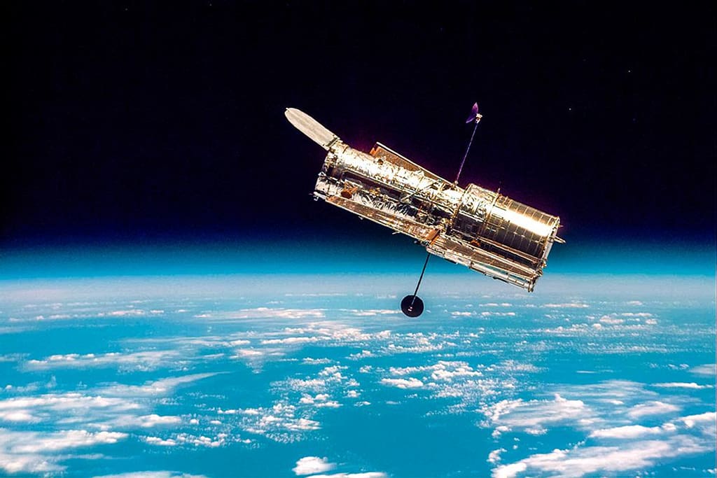 Telescópio Espacial Hubble em órbita da Terra, com o azul vibrante da atmosfera e a curvatura do planeta ao fundo, simbolizando sua posição estratégica fora da atmosfera.