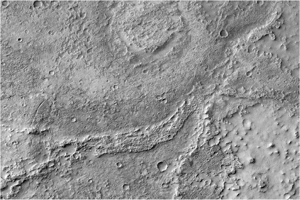 Uma crista fluvial sinuosa (FSR) moderadamente erodida, com vários pequenos crateras em sua superfície, que se destaca claramente acima do material circundante. A nordeste, ela surge de um pequeno vale e torna-se progressivamente mais visível em direção ao oeste, até desaparecer. Há uma curva evidente na FSR, provavelmente um meandro. Ao norte da FSR há uma formação arredondada e plana, provavelmente uma cratera de impacto que foi preenchida com água ou sedimento.
Imagem CTX: MurrayLab_V01_E020_N-20_Mosaic
NASA/JPL/MSSS/The Murray Lab