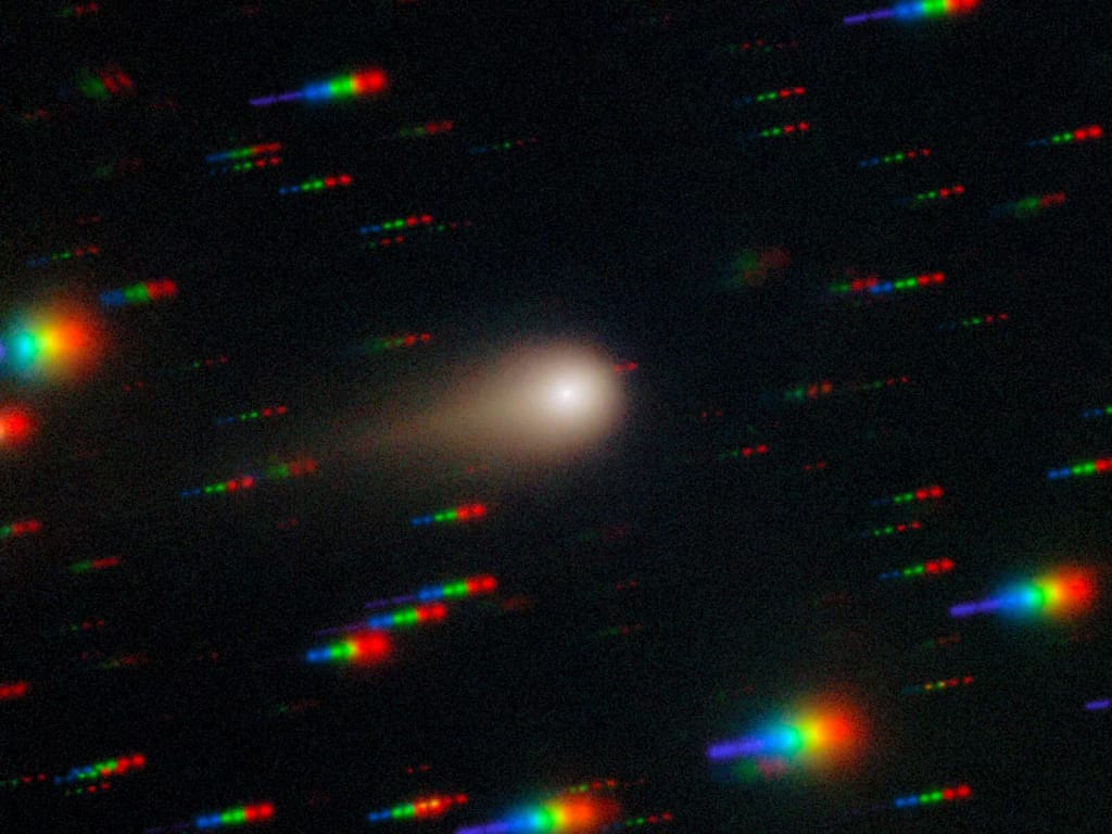 O cometa 3I/ATLAS risca um campo estelar denso nesta imagem capturada pelo Espectrógrafo Multiobjeto Gemini (GMOS) no telescópio Gemini South, localizado em Cerro Pachón, no Chile — uma das metades do Observatório Internacional Gemini, financiado em parte pela National Science Foundation (NSF) dos EUA e operado pelo NSF NOIRLab. A imagem é composta por exposições feitas através de quatro filtros — vermelho, verde, azul e ultravioleta. Durante as exposições, o cometa permanece fixo no centro do campo de visão do telescópio. No entanto, as posições das estrelas de fundo mudam em relação ao cometa, fazendo com que apareçam como rastros coloridos na imagem final. Essas observações do cometa 3I/ATLAS foram realizadas durante o programa Shadow the Scientists, organizado pelo NSF NOIRLab. Crédito: International Gemini Observatory/NOIRLab/NSF/AURA/Shadow the Scientist Processamento de imagem: J. Miller & M. Rodriguez (International Gemini Observatory/NSF NOIRLab), T.A. Rector (University of Alaska Anchorage/NSF NOIRLab), M. Zamani (NSF NOIRLab).