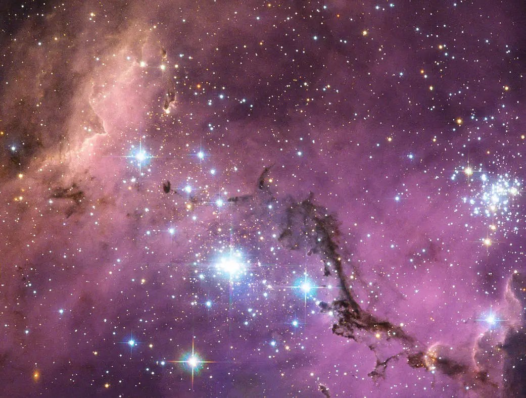 A cerca de 200 mil anos-luz da Terra, a Grande Nuvem de Magalhães — uma galáxia satélite da Via Láctea — flutua no espaço, em uma dança longa e lenta ao redor da nossa galáxia. Enormes nuvens de gás em seu interior colapsam lentamente, formando novas estrelas. Por sua vez, essas estrelas iluminam as nuvens de gás em um espetáculo de cores, visível nesta imagem do Telescópio Espacial Hubble.