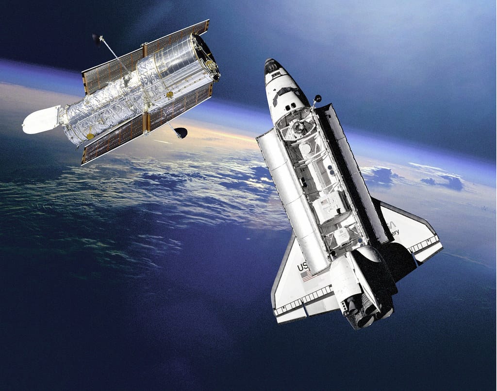 Imagem do Telescópio Espacial Hubble sendo lançado ao espaço pelo ônibus espacial Discovery em 1990. O Hubble revolucionou a astronomia com imagens detalhadas do universo, permitindo descobertas sobre galáxias distantes, buracos negros e a expansão do cosmos. Seu lançamento marcou um marco na exploração científica espacial.