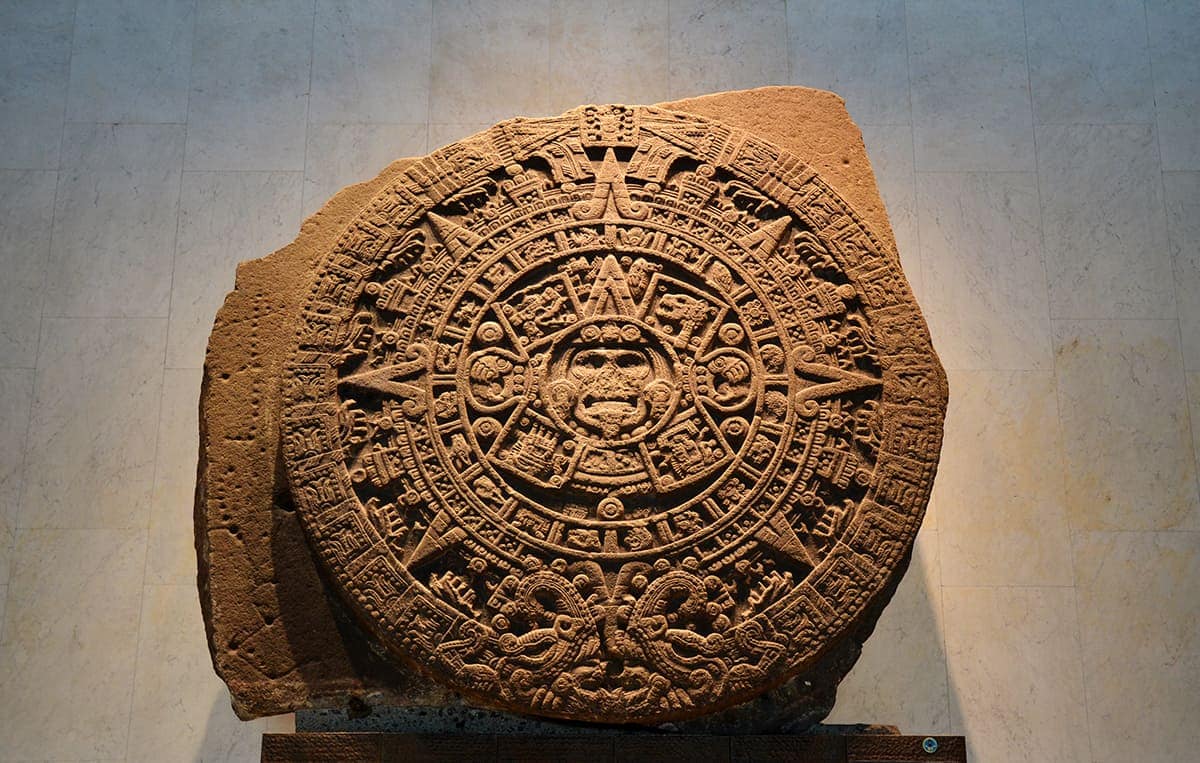alt="Pedra maia com inscrições representando a astronomia precisa desenvolvida pelos maias, documentando os movimentos da Lua, Sol, Vênus, Marte, a Via Láctea, e fenômenos como eclipses. As inscrições são detalhadas, demonstrando os cálculos matemáticos e observações feitas pelos maias."