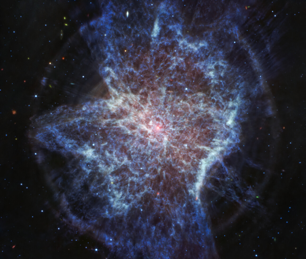 Imagem colorida, predominantemente azul, capturada em luz infravermelha média, mostrando uma nuvem luminosa com forma distorcida e assimétrica. No centro, uma estrela aparece como um pequeno ponto de luz branco-rosado. A forma irregular da nuvem em expansão de gás e poeira lembra tinta espalhada no chão. Os filamentos das camadas em expansão são delicados, com tons principalmente brancos e azulados. As camadas formam lóbulos que empurram o gás em direção ao plano equatorial, criando um disco. Um círculo quase perfeito de poeira azul-esbranquiçada contorna as bordas externas dessas camadas. O fundo da imagem é preto, pontilhado por pequenas estrelas brilhantes e galáxias distantes.