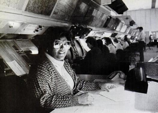 Imagem de Barbara A. Williams, primeira mulher afro-americana a obter Ph.D. em astronomia, com expressão confiante, cabelos escuros e blusa clara, ao fundo painéis de dados astronômicos.