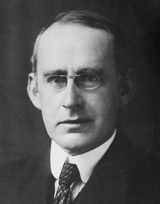 Retrato de Arthur Stanley Eddington, astrofísico britânico, conhecido por suas contribuições à relatividade geral e à física teórica. Na imagem, Eddington é visto com uma expressão séria e intelectual, vestindo roupas formais típicas da época. Ele é retratado como um homem de aparência madura, com cabelo claro e uma postura que reflete sua importância científica na astronomia e na física do século XX
