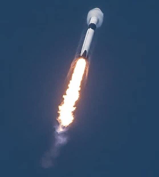 Foguete Falcon 9 quebrando a barreira do som, com os motores Merlin emitindo uma grande coluna de chamas. A imagem mostra claramente o cone de choque formado pela velocidade supersônica, com uma potente aceleração
