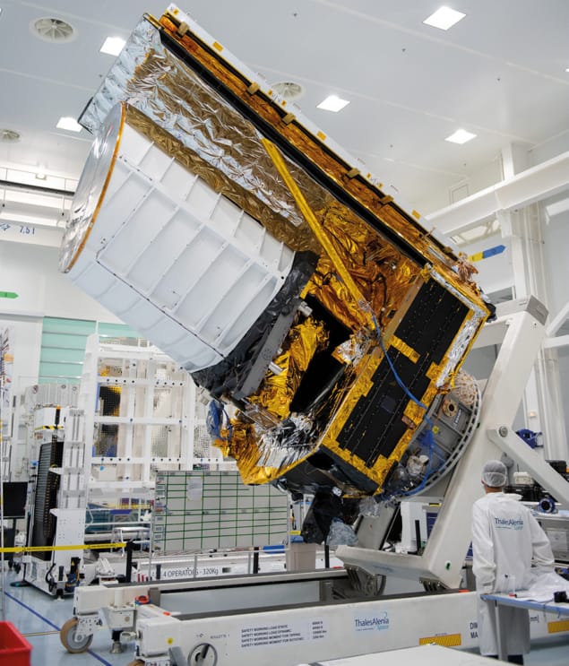 Fotografia do Telescópio Espacial Euclid em um laboratório antes do lançamento, cercado por cientistas com trajes especiais. O tamanho do telescópio, muito maior que os humanos ao redor, destaca a grandiosidade do projeto.