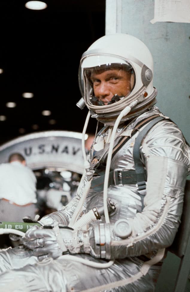 Fotografia de um astronauta famoso da NASA, já com o capacete e o traje espacial totalmente vestindo, característico da época. O traje, com seu design icônico, reflete a tecnologia espacial utilizada nas primeiras missões da NASA, destacando o pioneirismo da agência na exploração do espaço