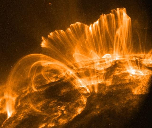 Explicação: Nesta imagem, a superfície do Sol aparece bastante escura. Um quadro de um filme registrado em 9 de novembro pelo telescópio orbital TRACE mostra loops coronais elevados sobre uma região ativa solar. Brilhando intensamente em luz ultravioleta extrema, o plasma quente, preso acima do Sol ao longo de campos magnéticos arqueados, está esfriando e “chovendo” de volta sobre a superfície solar.
Horas antes, em 8 de novembro, os astrônomos observaram essa mesma região ativa produzir uma erupção solar (flare) não tão espetacular. Mesmo assim, o flare de classe M liberou uma intensa tempestade de partículas, atingindo subitamente satélites próximos à Terra com prótons de alta energia.
O evento também foi associado a uma grande ejeção de massa coronal (CME), uma enorme nuvem de material que impactou o campo magnético da Terra cerca de 31 horas depois. O resultado foi uma forte tempestade geomagnética.