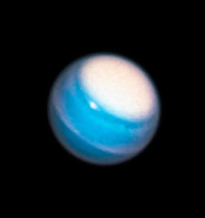 elescópio Hubble em 2011, mostrando Urano com uma névoa fotoquímica sobre o hemisfério norte. A névoa é visível, indicando o polo norte do planeta. O anel de Urano aparece em uma posição completamente diferente, completamente aberto, oferecendo uma visão única do planeta. A imagem destaca a complexidade e os mistérios de Urano, que ainda intrigam os cientistas e exigem sondas futuras para um estudo mais detalhado.