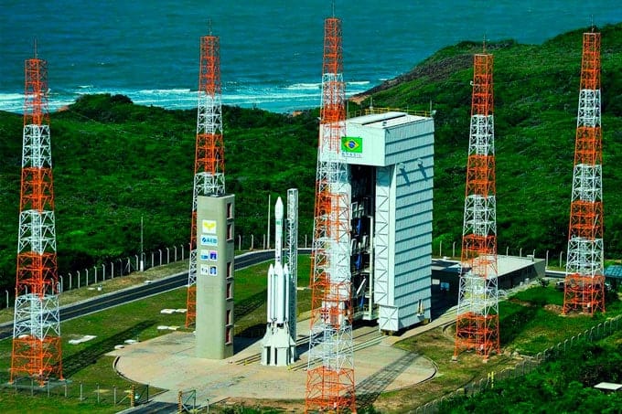 Vista da Base de Lançamento de Alcântara, localizada entre a floresta e o mar. A imagem mostra a infraestrutura de lançamento cercada por vegetação exuberante, com o vasto oceano ao fundo. Não é a  Base da NASA no Brasil,, mas é a Fachada do prédio da Agência Espacial Brasileira (AEB), com uma coloração azul escuro. Há uma marquise com o nome 'AGÊNCIA ESPACIAL BRASILEIRA' em letras garrafais e uma placa cromada com o logo da AEB. muitos acham que é uma  Base da NASA no Brasil, mas na verdade a base é brasileira.