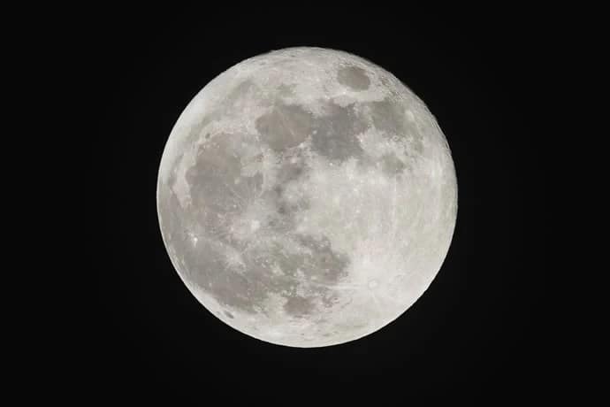 Lua na fase cheia, iluminada de maneira intensa e clara, com detalhes visíveis de suas crateras e mares lunares. O céu ao fundo é de um tom profundo de preto, destacando a beleza e a magnitude da Lua em seu esplendor.