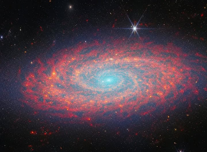 galáxia NGC 2090 capturada pela NASA. A galáxia, localizada a cerca de 100 milhões de anos-luz da Terra, exibe uma estrutura espiral com cores vibrantes, com áreas de formação estelar em tons de azul e roxo, contrastando com o fundo escuro do espaço profundo. O brilho das estrelas jovens e das regiões de gás e poeira é claramente visível, destacando a complexidade e beleza da galáxia.