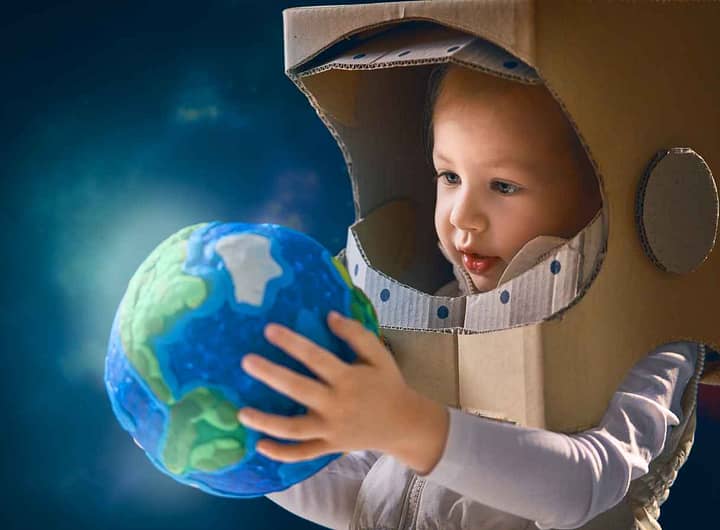 Criança com traje de astronauta, segurando uma réplica do planeta Terra, ilustrando a importância da astronomia no ensino fundamental e despertando o interesse pela ciência espacial.