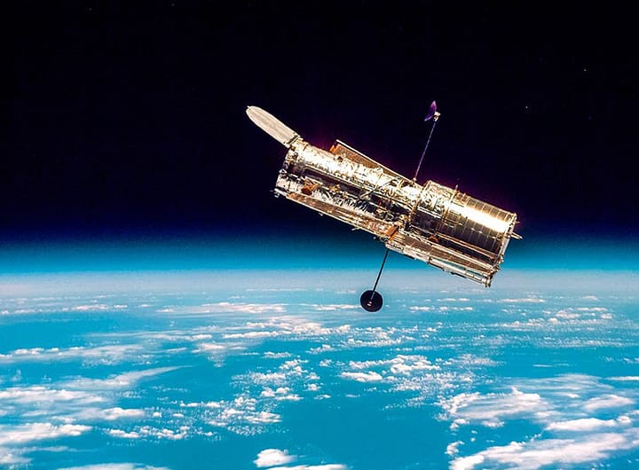Telescópio Espacial Hubble em órbita da Terra, com o azul vibrante da atmosfera e a curvatura do planeta ao fundo, simbolizando sua posição estratégica fora da atmosfera.