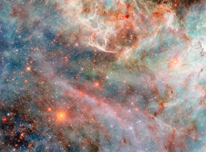 Parte de uma nebulosa no espaço. Camadas de gás e nuvens de poeira em diferentes cores — variando de tons de azul e verde a rosa, vermelho e preto — compõem a nebulosa, indicando a luz emitida por diferentes moléculas. As camadas de nuvens ao fundo são mais espessas e volumosas, embora ainda translúcidas, enquanto as camadas superiores são finas e brilhantes nas bordas. Atrás das nuvens, há muitas estrelas pequenas, em sua maioria alaranjadas e algumas azuis.