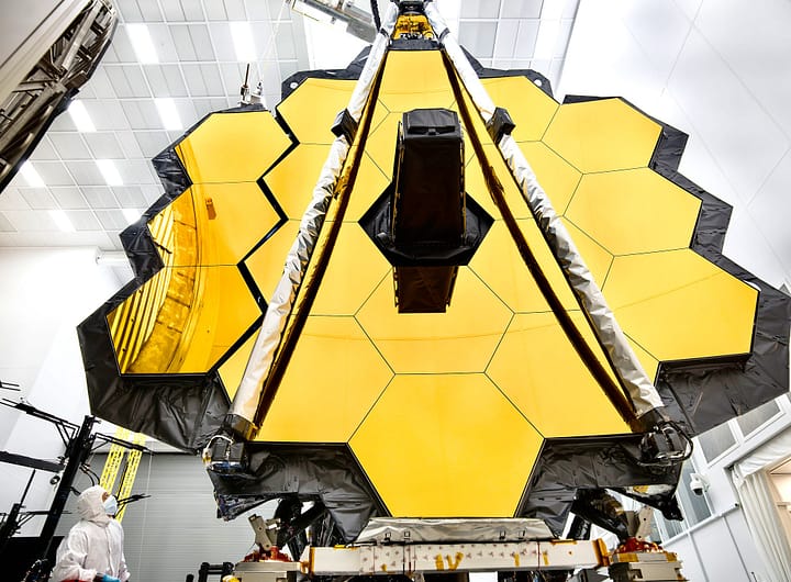 O imponente espelho primário do Telescópio Espacial James Webb da NASA está dentro de uma sala limpa no Centro Espacial Johnson da NASA, em Houston, onde passará por seu último teste criogênico antes de ser lançado ao espaço em 2018. Em preparação para o teste, as "asas" do espelho (que consistem em três segmentos de cada lado) foram abertas. Esta foto mostra uma asa totalmente desdobrada e outra que está a momentos de se desdobrar completamente. Um engenheiro observa o movimento. O Telescópio Espacial James Webb é o observatório espacial mais avançado do mundo. Esta maravilha da engenharia foi projetada para desvendar alguns dos maiores mistérios do universo, desde a descoberta das primeiras estrelas e galáxias que se formaram após o Big Bang até o estudo das atmosferas de planetas ao redor de outras estrelas. É um projeto conjunto da NASA, da ESA (Agência Espacial Europeia) e da Agência Espacial Canadense.