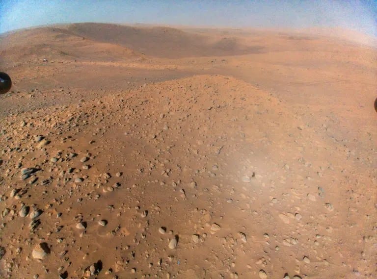O Perseverance, da NASA, pousou acompanhado pelo helicóptero Ingenuity, que comprovou que voar na atmosfera rarefeita de Marte era possível. Esta imagem feita pelo Ingenuity — capturada de uma altitude de cerca de 12 metros durante seu 51º voo — mostra o rover, visível como um ponto esbranquiçado no canto superior esquerdo.
NASA/JPL-Caltech