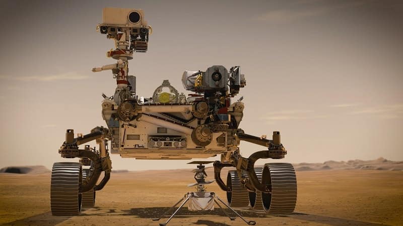Representação artística de uma selfie do rover Perseverance em Marte, com o helicóptero Ingenuity no solo marciano ao fundo. O Perseverance, enviado pela NASA, explora a superfície do planeta em busca de sinais de vida passada, enquanto o Ingenuity testa a capacidade de voos em outro mundo.