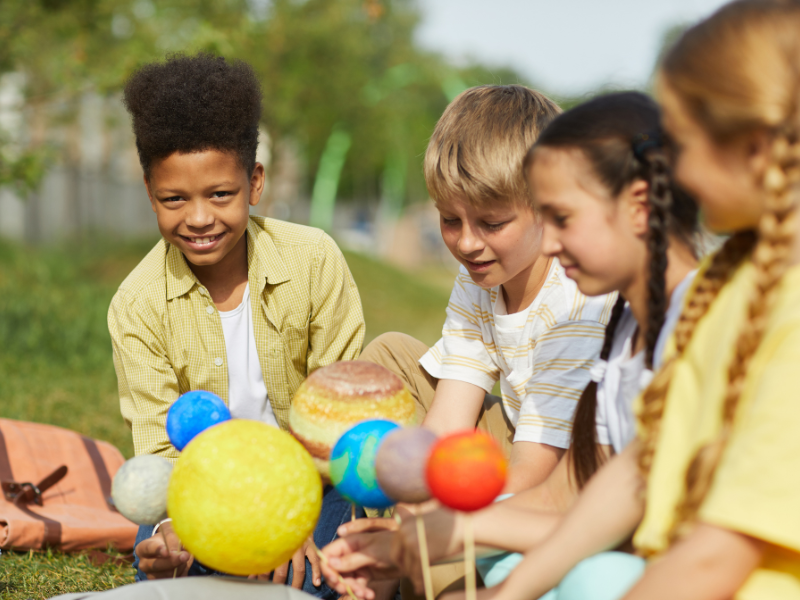 Crianças brincando e aprendendo astronomia infantil com planetas em miniatura