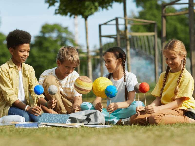 Alunos explorando astronomia infantil ao ar livre com modelo do sistema solar
