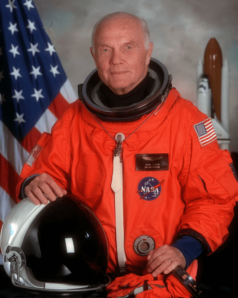 Fotografia oficial recente de um astronauta famoso da NASA, agora idoso, com cabelos brancos. Ele está usando o traje espacial laranja típico das missões mais recentes da NASA, refletindo a continuidade de sua contribuição para a exploração espacial ao longo dos anos