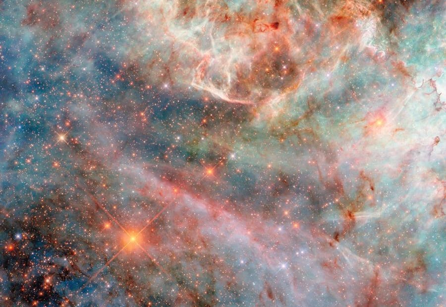 Parte de uma nebulosa no espaço. Camadas de gás e nuvens de poeira em diferentes cores — variando de tons de azul e verde a rosa, vermelho e preto — compõem a nebulosa, indicando a luz emitida por diferentes moléculas. As camadas de nuvens ao fundo são mais espessas e volumosas, embora ainda translúcidas, enquanto as camadas superiores são finas e brilhantes nas bordas. Atrás das nuvens, há muitas estrelas pequenas, em sua maioria alaranjadas e algumas azuis.