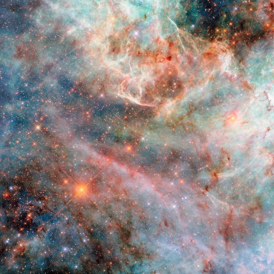 Parte de uma nebulosa no espaço. Camadas de gás e nuvens de poeira em diferentes cores — variando de tons de azul e verde a rosa, vermelho e preto — compõem a nebulosa, indicando a luz emitida por diferentes moléculas. As camadas de nuvens ao fundo são mais espessas e volumosas, embora ainda translúcidas, enquanto as camadas superiores são finas e brilhantes nas bordas. Atrás das nuvens, há muitas estrelas pequenas, em sua maioria alaranjadas e algumas azuis.