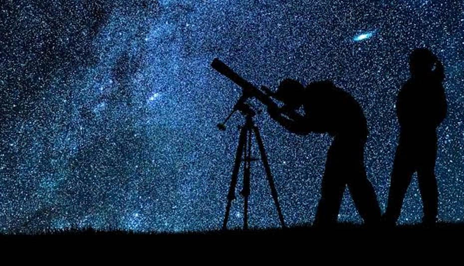 Silhueta de um homem e uma mulher, com a mulher de cabelo longo e a mão no bolso, ambos observando o céu estrelado com um telescópio, ilustrando o conceito de 'O que é um astrônomo'O que é astronomia