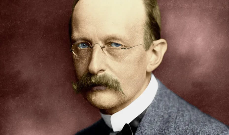 Max Planck, com olhos claros, bigode e óculos, exalando um olhar sério. Ele está vestido com um terno cinza e gravata preta, capturando sua postura de autoridade e intelectualidade.