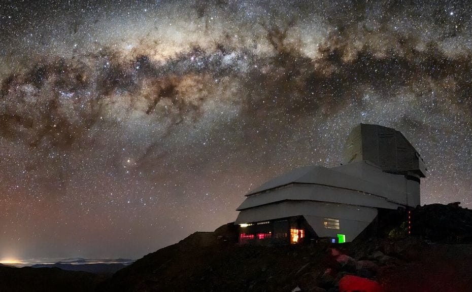 Observatório Vera C. Rubin sob um céu noturno repleto de estrelas e a Via Láctea visível ao fundo, no Cerro Pachón, Chile.