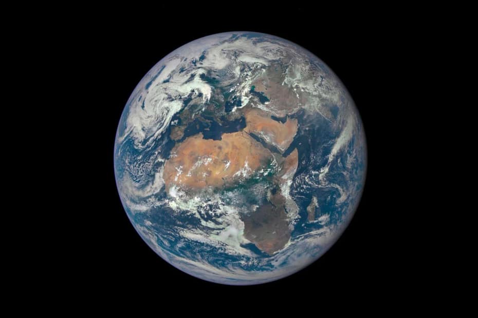 Imagem do Planeta Terra vista do espaço, destacando os continentes e oceanos. A atmosfera azul e as nuvens brancas são visíveis ao redor, com a luz solar iluminando parcialmente o lado do planeta.