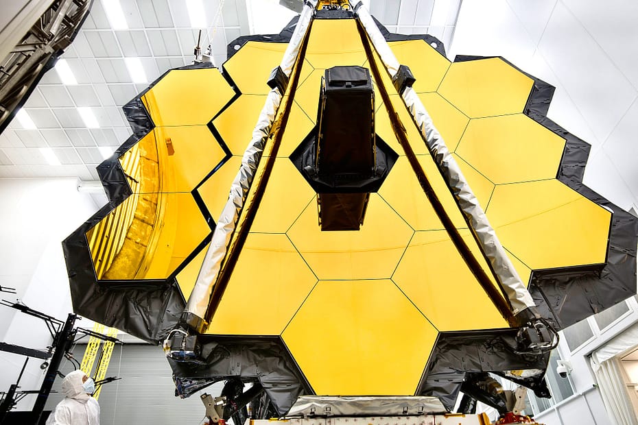 O imponente espelho primário do Telescópio Espacial James Webb da NASA está dentro de uma sala limpa no Centro Espacial Johnson da NASA, em Houston, onde passará por seu último teste criogênico antes de ser lançado ao espaço em 2018. Em preparação para o teste, as "asas" do espelho (que consistem em três segmentos de cada lado) foram abertas. Esta foto mostra uma asa totalmente desdobrada e outra que está a momentos de se desdobrar completamente. Um engenheiro observa o movimento. O Telescópio Espacial James Webb é o observatório espacial mais avançado do mundo. Esta maravilha da engenharia foi projetada para desvendar alguns dos maiores mistérios do universo, desde a descoberta das primeiras estrelas e galáxias que se formaram após o Big Bang até o estudo das atmosferas de planetas ao redor de outras estrelas. É um projeto conjunto da NASA, da ESA (Agência Espacial Europeia) e da Agência Espacial Canadense.