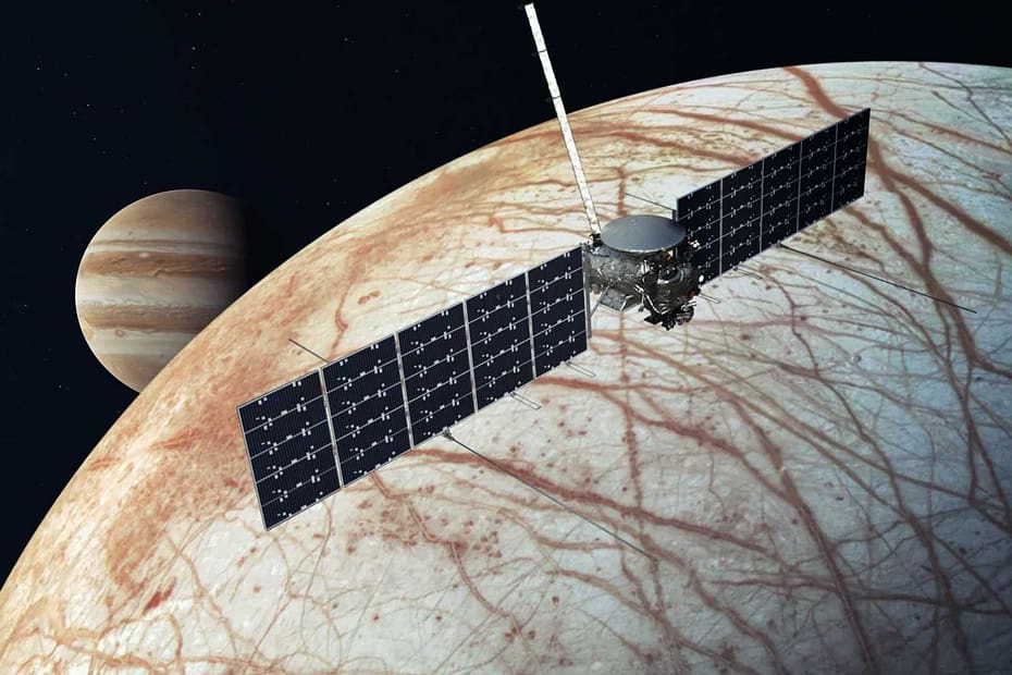 alt="Uma nave espacial paira sobre uma lua listrada avermelhada com o planeta Júpiter ao fundo."