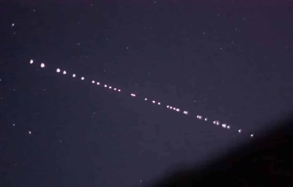 Fotografia real de satélites Starlink em órbita, visíveis no céu noturno como uma linha de pontos brilhantes, formando um padrão semelhante a um 'trenzinho'. A imagem mostra os satélites da SpaceX enquanto viajam em conjunto, iluminando o céu escuro. Esse fenômeno é uma visão única e impressionante da constelação de satélites Starlink em movimento, conectando a Terra com sua rede global de internet via satélite.