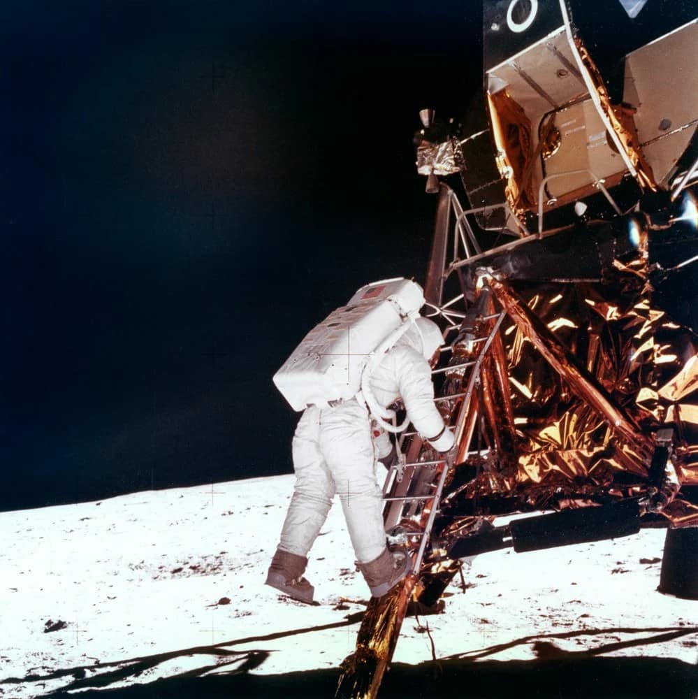 Imagem icônica de Buzz Aldrin descendo do módulo lunar Eagle durante a missão Apollo 11, em 1969. Ele está de traje espacial completo, com os pés quase tocando a superfície lunar pela primeira vez. A foto, tirada por Neil Armstrong, simboliza um dos momentos mais históricos da exploração espacial, quando o homem pisou pela primeira vez na Lua