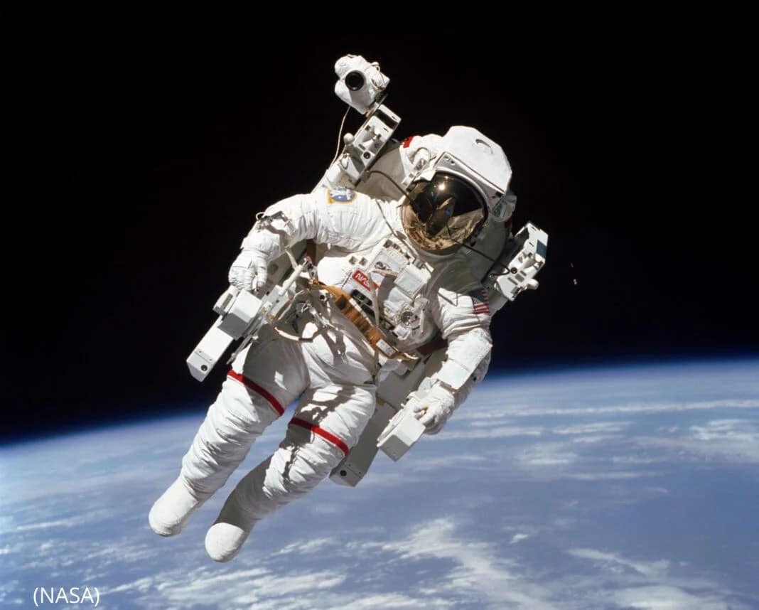 Bruce McCandless II flutuando no espaço durante a missão STS-41-B do ônibus espacial Challenger, em fevereiro de 1984. Ele está usando um traje espacial, sem estar preso à nave-mãe, representando a primeira caminhada no espaço livre. Ao fundo, o vasto e escuro espaço sideral, com a Terra parcialmente visível abaixo, e as estrelas pontilhando o céu esse é um dia-a-dia de Quem trabalha no espaço