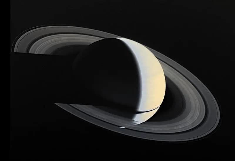 Imagem de Saturno e seus anéis tirada pela Voyager 1 em 16 de novembro de 1980, quatro dias após a maior aproximação do planeta, a uma distância de 5.300.000 km (3.300.000 milhas). Essa geometria de visualização, que mostra Saturno em forma de crescente, nunca é alcançada a partir da Terra. Os anéis de Saturno, assim como o topo das nuvens do próprio planeta, são visíveis porque refletem a luz do Sol. A natureza translúcida dos anéis é evidente onde Saturno pode ser visto através de partes deles. Outras partes dos anéis são tão densas com partículas de gelo em órbita que quase nenhuma luz solar passa por elas, projetando uma sombra sobre o topo amarelado das nuvens de Saturno, que por sua vez projeta uma sombra sobre os anéis à direita. A faixa preta dentro dos anéis é a Divisão de Cassini, que contém muito menos material em órbita do que o restante dos anéis.
Crédito da imagem: NASA/JPL-Caltech