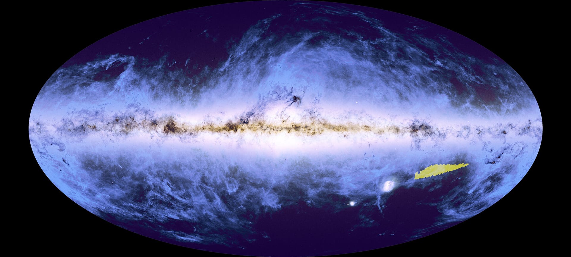 Uma imagem oval azul escura, com uma faixa brilhante que se estende da esquerda para a direita, de onde nuvens azul-claras parecem se espalhar pelo restante da forma. Essa faixa brilhante é interrompida por estruturas mais escuras, semelhantes a nuvens. No canto inferior direito da oval, há uma pequena área destacada em amarelo brilhante, indicando a localização do mosaico completo no contexto deste mapa global da nossa galáxia, a Via Láctea.