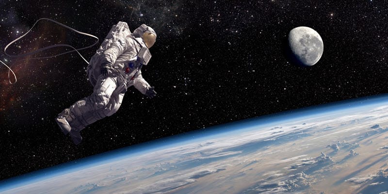 Astronauta flutuando no espaço com a Terra abaixo e indo em direção à Lua, representando a astronomia na exploração espacial.

